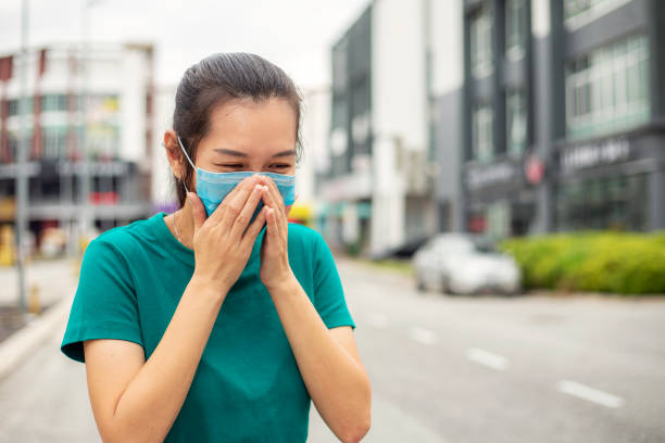 mulher usa máscara facial e espirra enquanto está na cidade - smog city pollution town - fotografias e filmes do acervo