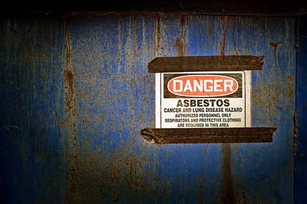 A sign warns of danger from asbestos contamination and the need for protective clothing.