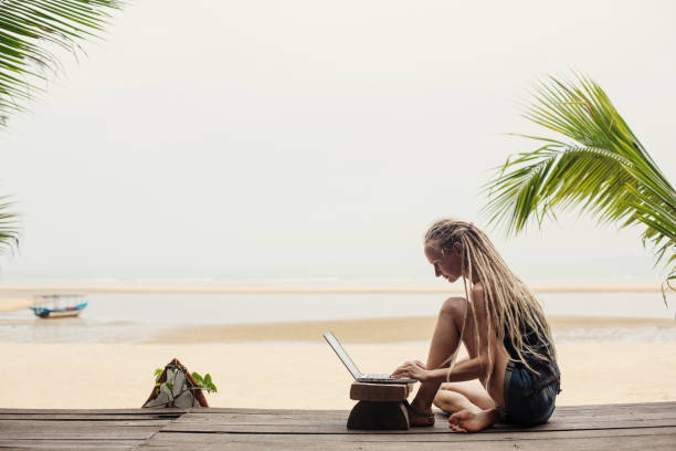 istock Young female wearing dreadlocks using laptop on sea shore. Shopping online, freelance, working outdoor 1205905077