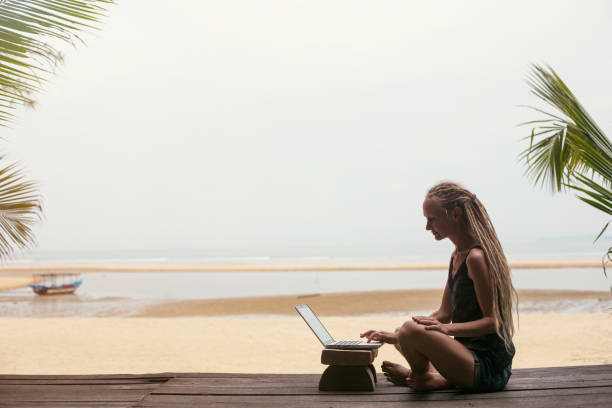 istock Young female wearing dreadlocks using laptop on sea shore. Shopping online, freelance, working outdoor 1205906409