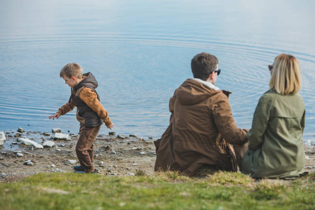 família andando perto da água. sentado na praia. criança jogando pedra na água - throwing stone little boys child - fotografias e filmes do acervo