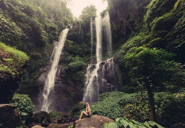 istock Young woman seating near jungle waterfall 1205912825