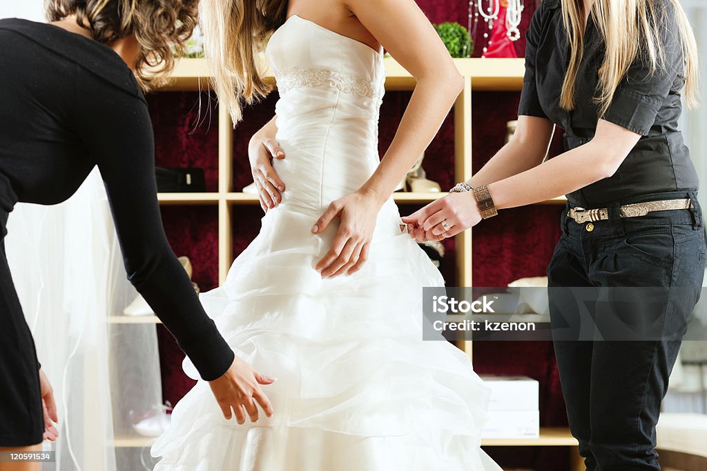 A bride fitting her wedding dress in the shop Bride at the clothes shop for wedding dresses; she is choosing a dress and the designer are assisting her Measuring Stock Photo