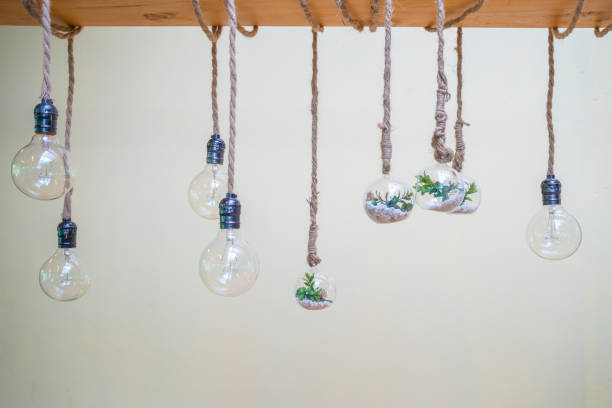 istock Decorated cozy lamps stick in the rope and little tiny tree with small white rock inside the ball glass hang on to big wood log in front of white background. 1205916775