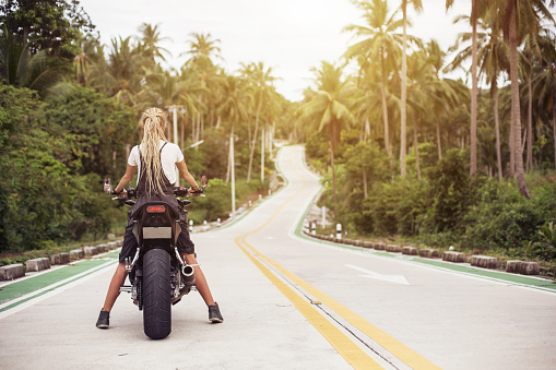 Portrait of female Biker sitting on big motorcycle. Girl driver with dread locks, travel way concept