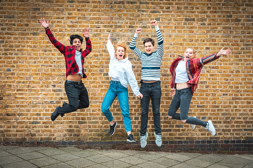 Happy teen friends jumping in front of a wall in London - Multiracial group of teenagers best friends enjoying time together and having fun - Lifestyle and friendship in London