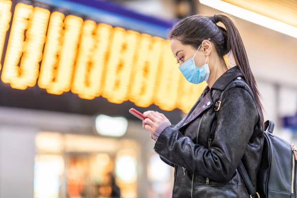Chinese woman wearing face mask at train station Chinese woman wearing face mask at train station to protect from smog and virus - young asian woman looking at her smartphone with departure arrivals board behind - health and travel concepts central london photos stock pictures, royalty-free photos & images