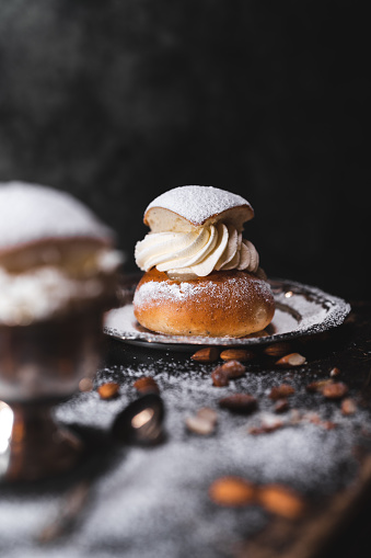 A traditional baked dessert from Sweden knows as a semla on a wooden table, surrounded by almonds. Served on metal plates.