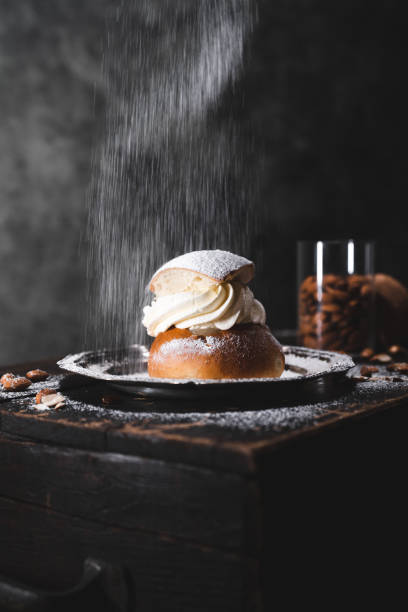 Traditional Swedish dessert known as semla with almonds A traditional baked dessert from Sweden knows as a semla on a wooden table, surrounded by almonds. Served on metal plates. sprinkling powdered sugar stock pictures, royalty-free photos & images