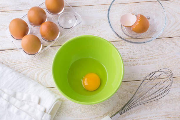 istock One raw egg in a green bowl, five brown chicken eggs in a transparent plastic tray and  stainless steel whisk on a white wooden table. Cooking for easter. 1205918516