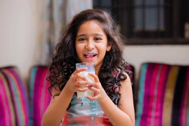 portrait of a cheerful cute girl smiling holding a glass of milk stock photo - milk mustache imagens e fotografias de stock
