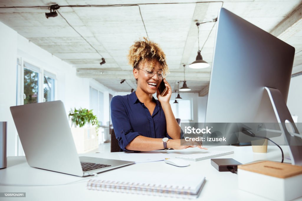 Businesswoman dealing with client through phone Smiling businesswoman dealing with client through smart phone. Female financial expert is working in creative office. She is related to financial occupation. Laptop Stock Photo