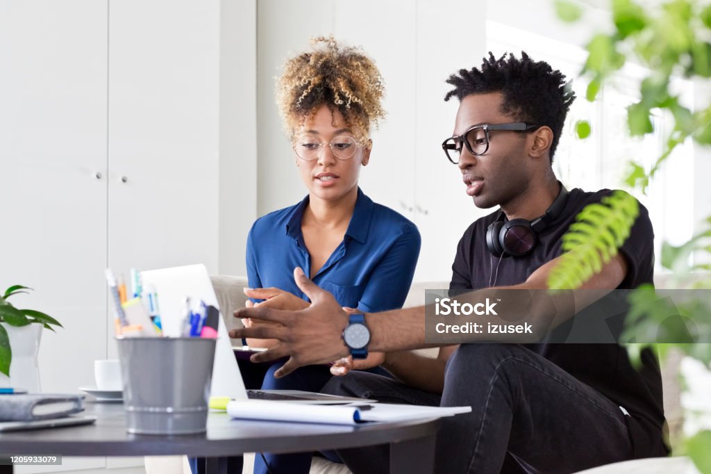 Colleagues discussing over laptop at office Confident entrepreneurs discussing over laptop at table. Male and female colleagues are sitting at creative workplace. They are in smart casuals in office. 30-34 Years Stock Photo