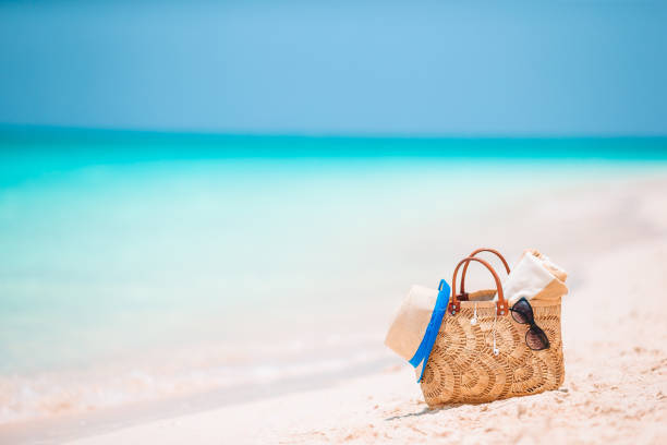 Beach accessories - bag, straw hat, sunglasses on white beach
