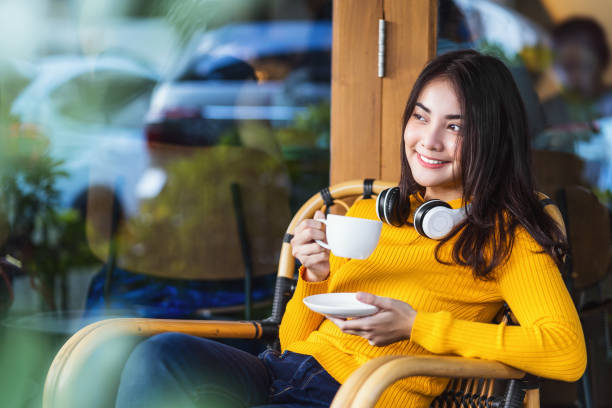 jeune femelle asiatique retenant une tasse de café et s’asseyant dans le café moderne - coffee shop coffee break coffee cup holding photos et images de collection