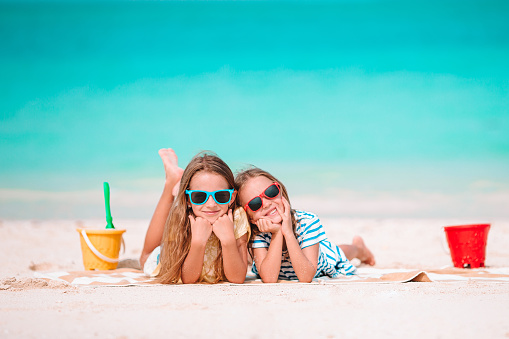 Little happy funny girls have a lot of fun at tropical beach playing together and making sand castle