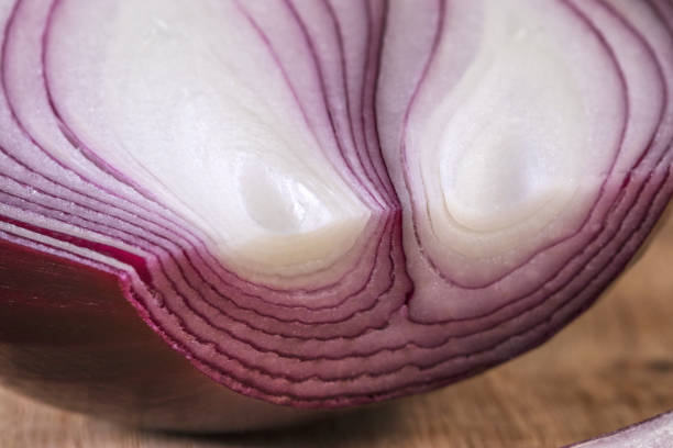 Red onion is cut in half and lies on a white oak kitchen board, with artificial lighting. Still life for the kitchen or element of the vegetarian menu.
