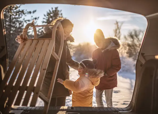 Mother and her boys getting out of car trunk sleds on winter holiday