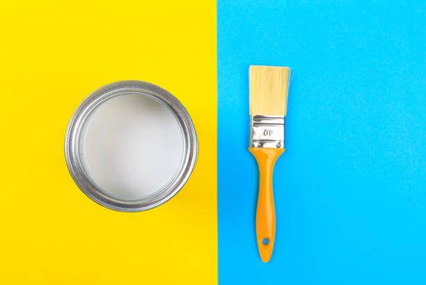 istock White Paint Can with Brush Top View On Yellow and blue  Background. 1205949372