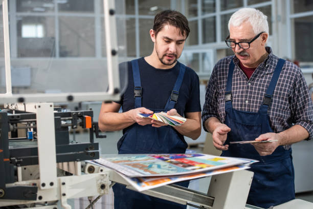 Choosing colors for printing Busy printing plant workers standing at printed pages and choosing colors for next printing digital printing house stock pictures, royalty-free photos & images