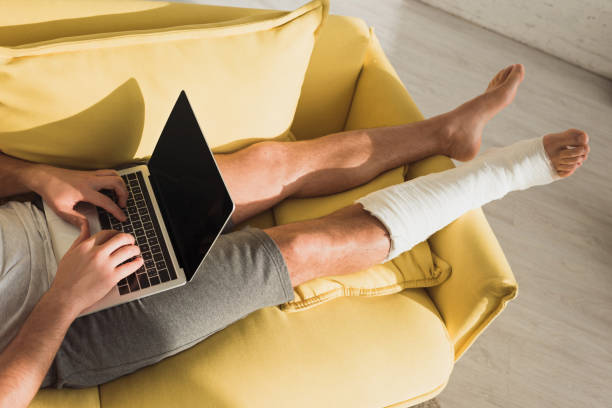 Cropped view of freelancer with leg in plaster bandage using laptop on sofa at home Cropped view of freelancer with leg in plaster bandage using laptop on sofa at home broken leg stock pictures, royalty-free photos & images