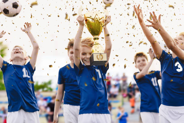 чемпион молодежной футбольной команды с выигрышным трофеем. мальчики футбольной команды празднуют победу в школьных соревнованиях, подни� - child celebration cheering victory стоковые фото и изображения