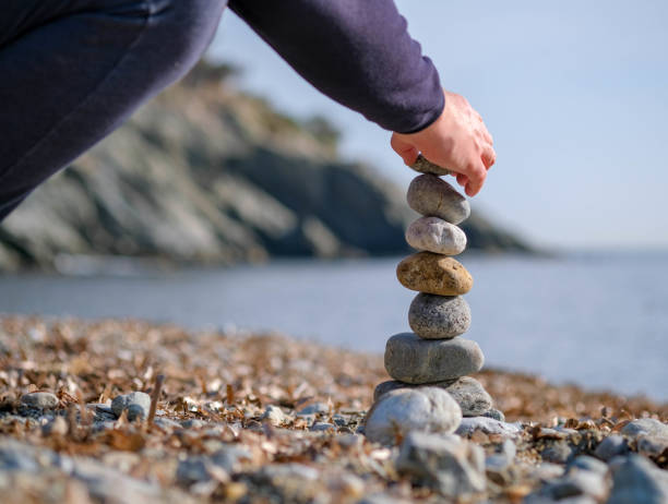 istock Young man's hand lays a stone on a stone cairn on the beach 1205963732