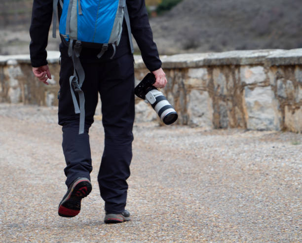 istock Man holding a camera with a big zoom objective outdoors in the middle of a path surrounded by a stone wall 1205964994