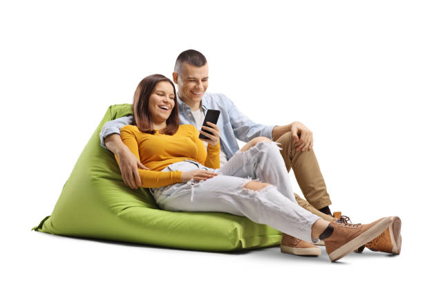 Smiling young couple sitting on a green bean bag and looking at a mobile phone Smiling young couple sitting on a green bean bag and looking at a mobile phone isolated on white background bean bag stock pictures, royalty-free photos & images