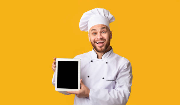 istock Happy Chef Showing Digital Tablet Screen On Yellow Studio Background 1205975611