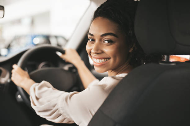 feliz mujer afroamericana sentada en el auto en el centro de concesionarios - conducir fotografías e imágenes de stock