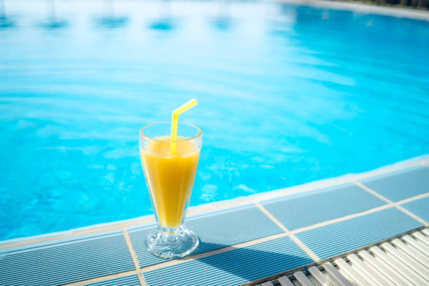istock Glass of juice on swimming pool edge 1205977100