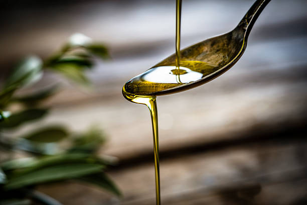 Pouring extra virgin olive oil Pouring extra virgin olive oil on a vintage metal spoon. Selective focus on spoon. Useful copy space available for text and/or logo. Predominant colors are gold, green and brown. High resolution 42Mp studio digital capture taken with Sony A7rii and Sony FE 90mm f2.8 macro G OSS lens cooking oil photos stock pictures, royalty-free photos & images