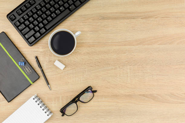 istock Office desk table with computer keyboard,coffee,glasses and  blank notebook. Top view with copy space on wooden background. 1205982544