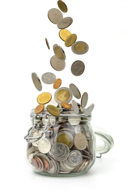 Coins falling on pile of money into glass jar on white background .Saving money for business and financial concept.Save for retirement planning.
