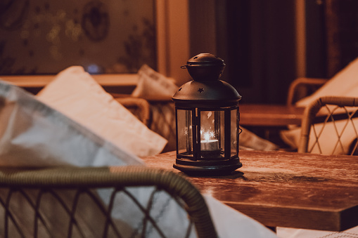 Close up of a candle lamp on an outdoor table at night, cosy atmosphere, selective focus.