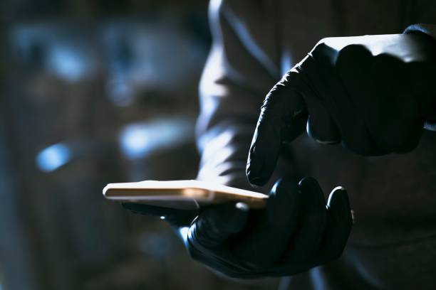 istock hacker in the hood working with mobile phone typing text in dark room 1205989169
