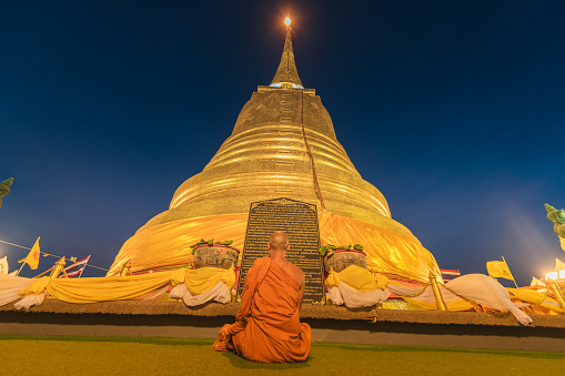 Bangkok, Thailand - April 20 2019: Monk sitting and praying in front of Budda statue and pagoda inside Wat Saket, or Golden Mount.