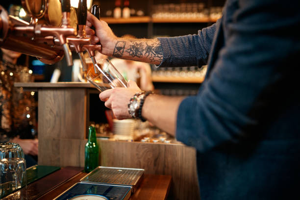 istock Tattooed caucasian barman pouring beer while standing in pub. Selective focus on hand. 1205991652