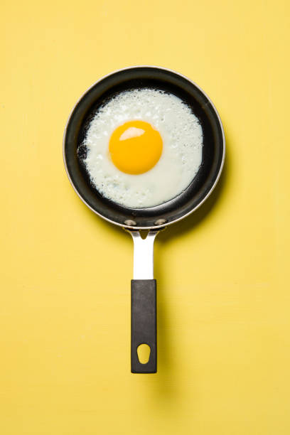 Egg in a pan on yellow background - fotografia de stock