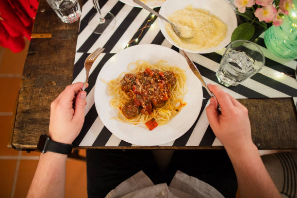 A directly above shot of a plate of spaghetti meatballs on a dining table, an unrecognizable person is about to eat them.