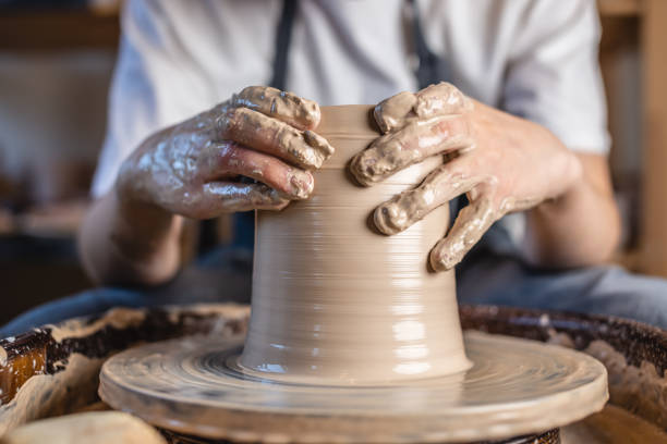 istock Potter working on a Potter's wheel making a vase. Woman forming the clay with hands creating jug in a workshop. Close up 1205993528