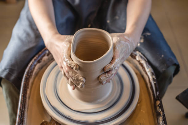 istock Woman potter working on Potter's wheel making a vase. Master forming the clay with her hands creating jug in a workshop 1205993805