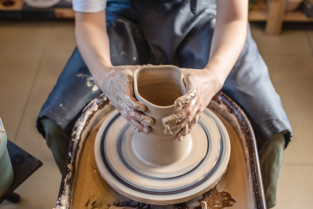istock Woman potter working on Potter's wheel making a vase. Master forming the clay with her hands creating jug in a workshop 1205993822