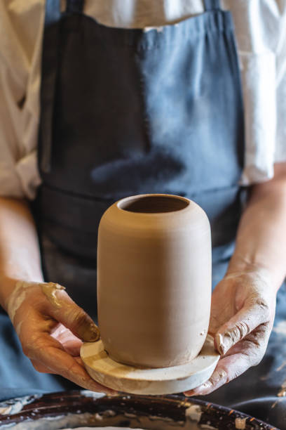 istock Woman potter working on a Potter's wheel making a vase. Master pulls the jug off the circle gently holding it in hands 1205993986