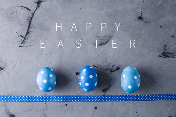 istock Three bright blue polka dot eggs with a ribbon on a gray background. Festive Easter card 1205996181