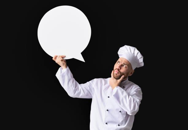 istock Puzzled Chef Holding White Speech Bubble Standing Over Black Background 1206000595