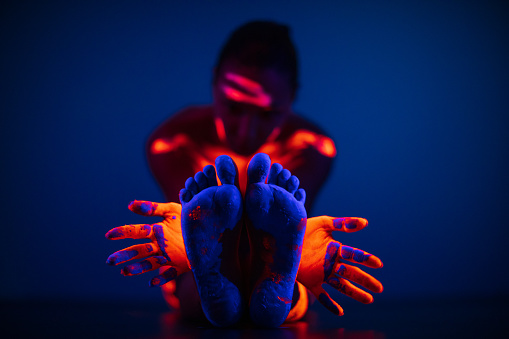 Portrait of young woman with body painted with fluorescent makeup that glowing under the ultraviolet light. Photo taken under the real neon ultraviolet light (black light). High ISO value