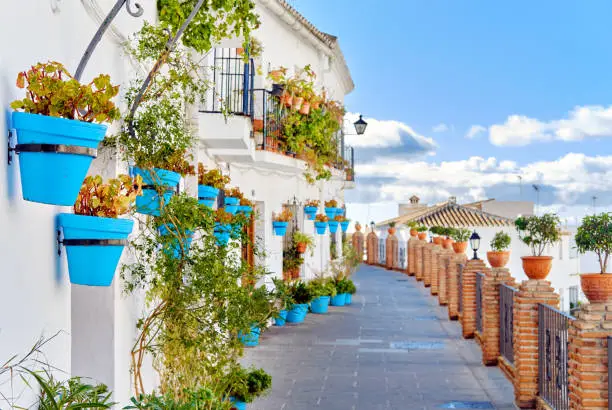 Idyllic scenery empty picturesque street of small white-washed village of Mijas. Path way decorated with hanging plants in bright blue flowerpots, Costa del Sol, Andalusia, Province of Málaga, Spain