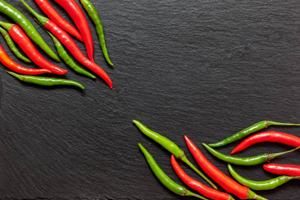 Fresh spicy red and green pepper on a slate board, various colorful chili peppers and cayenne peppers on dark background from above. Top view, copy space. stock photo